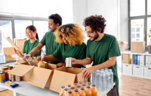 A group of happy smiling volunteers packing food in boxes according to list on clipboard at an assistance center.