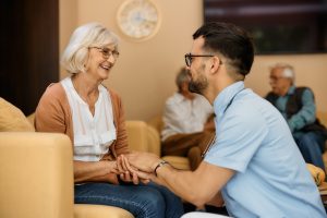 Male caregiver and senior woman hold hands while communicating at residential care home.